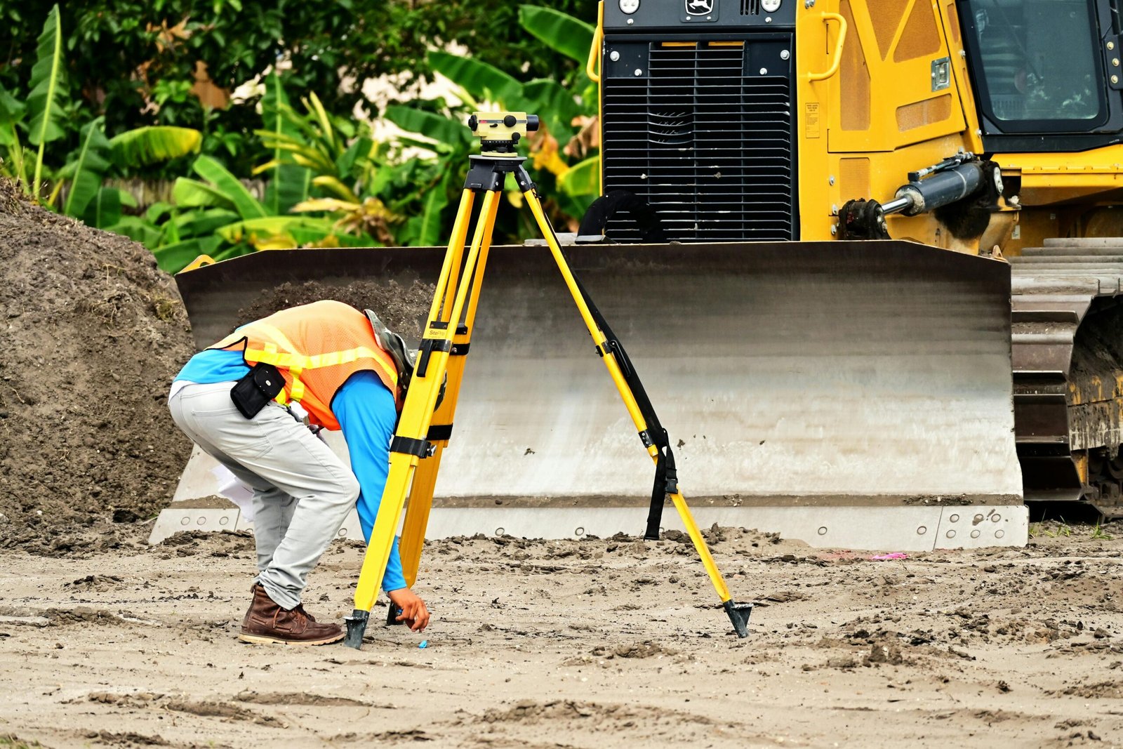 About A construction worker operates a total station in front of a bulldozer on a construction site.